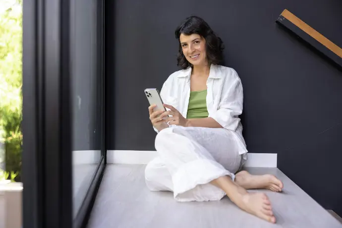 a woman sitting on a window sill looking at her cell phone