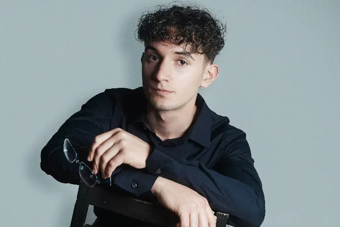a young man sitting in a chair holding a pair of glasses